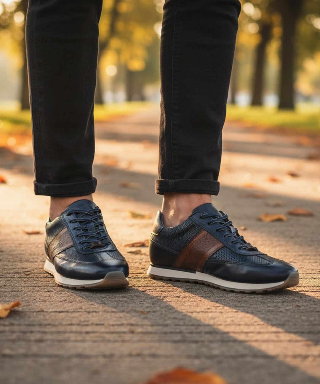 bugatti Ivar dark blue leather sneakers with brown stripe, white midsole, worn with black jeans.
