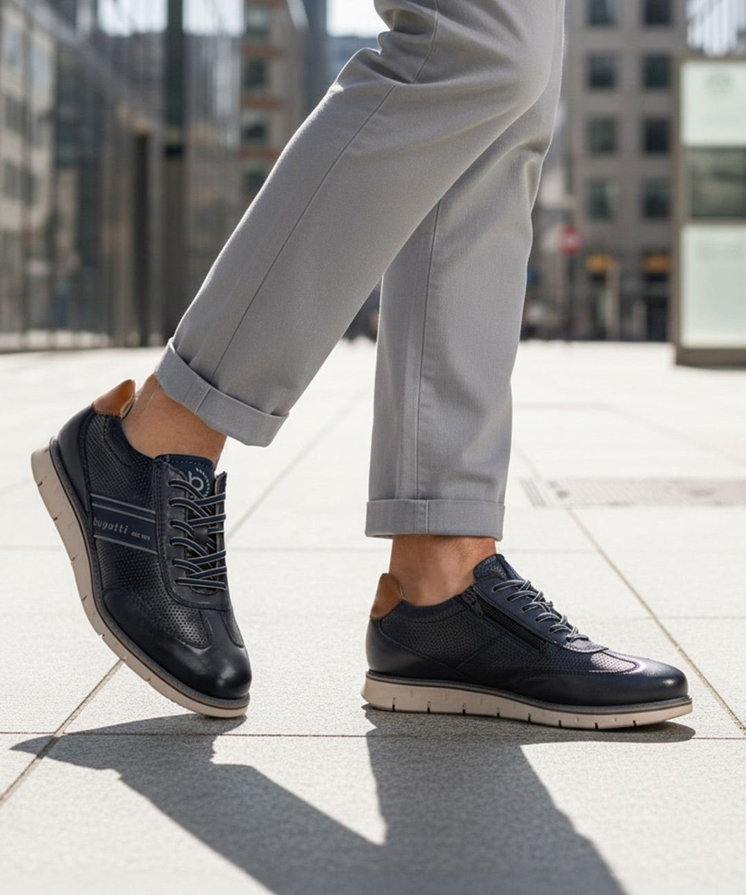 Lifestyle shot of bugatti Sprinter dark blue leather sneakers with light soles, paired with gray casual pants.
