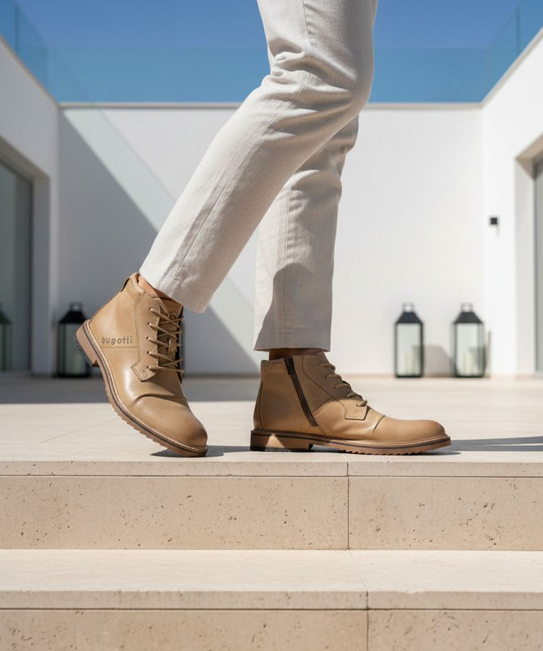 Lifestyle shot of Bugatti Baldor boots in sand-colored leather, featuring a side zipper and lace-up closure, paired with light-colored trousers.
