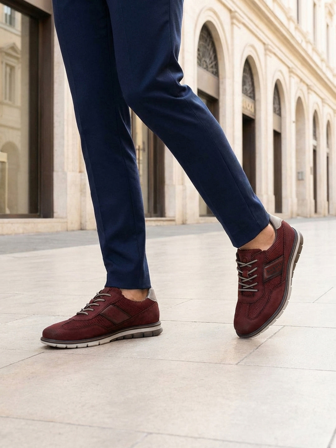 Cropped lifestyle image of bugatti Simone Comfort dark red leather casual shoes with grey soles, worn with blue trousers.
