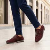 Cropped lifestyle image of bugatti Simone Comfort dark red leather casual shoes with grey soles, worn with blue trousers.
