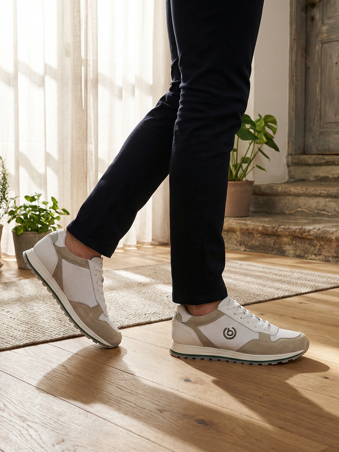 Lifestyle shot of bugatti Garnet Evo Sand Premium Leather Comfort Sneakers, paired with dark trousers, and set on a wood floor.