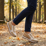 Lifestyle shot of bugatti Garnet Evo Sand sneakers in leather and suede, styled with navy trousers while walking on a path.