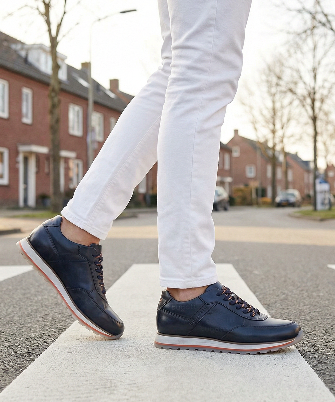 Lifestyle view of bugatti Garnet Evo dark blue leather sneakers with orange laces on a crosswalk.
