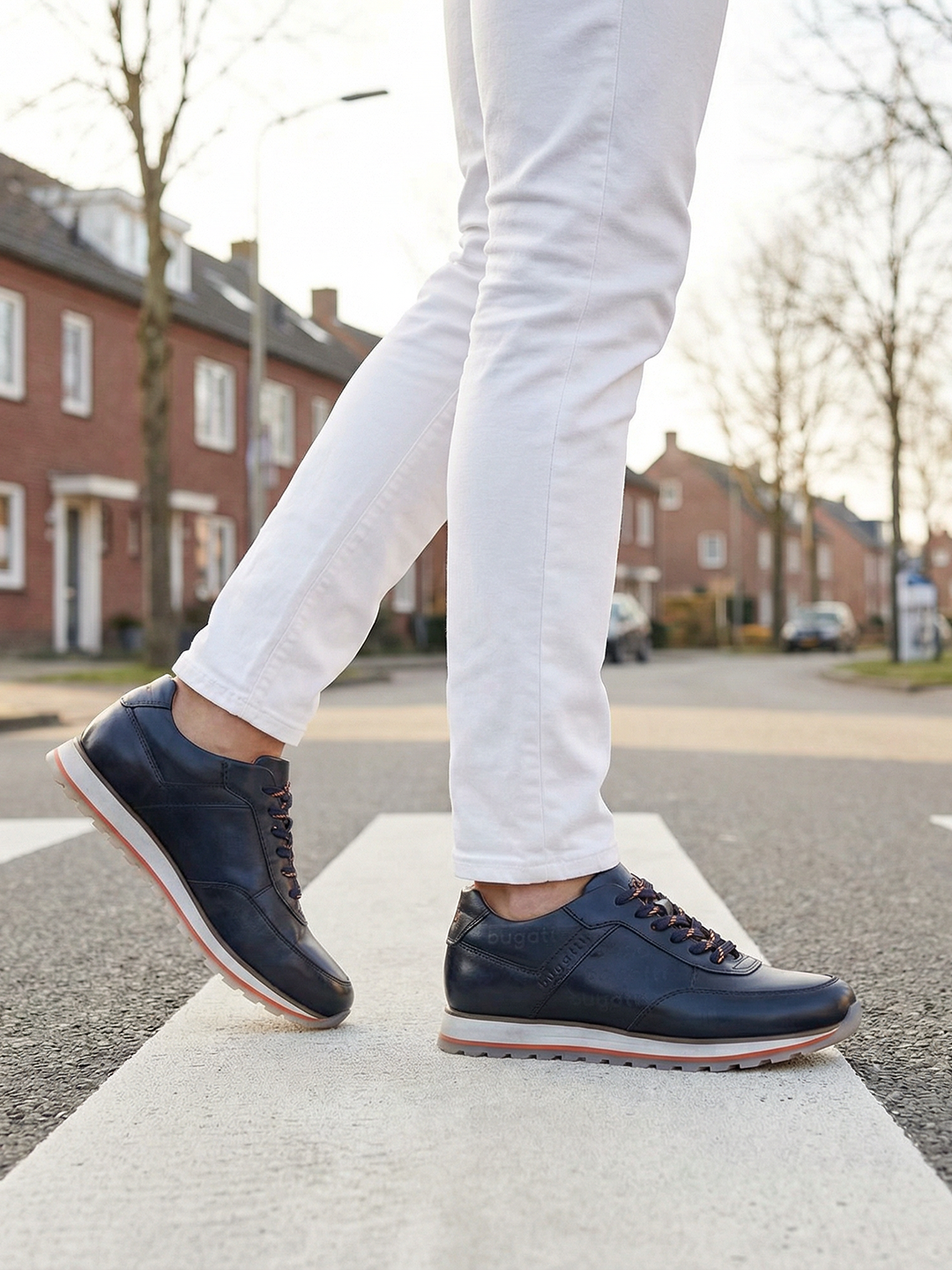 Lifestyle view of bugatti Garnet Evo dark blue leather sneakers with orange laces on a crosswalk.
