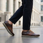 Lifestyle view of bugatti Garnet Evo dark brown premium leather sneakers with dark pants on a city street.