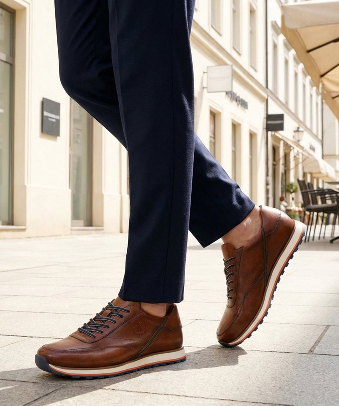 Lifestyle image of bugatti Garnet Evo cognac leather sneakers with white soles, worn with dark blue pants.