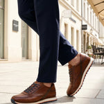 Lifestyle image of bugatti Garnet Evo cognac leather sneakers with white soles, worn with dark blue pants.