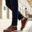 Lifestyle image of bugatti Garnet Evo cognac leather sneakers with white soles, worn with dark blue pants.