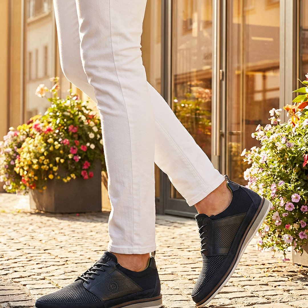 Lifestyle close-up of bugatti Sione Comfort dark blue casual shoes worn with white pants.
