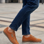 Cropped shot of a person wearing bugatti Makkor orange casual shoes with blue jeans on a concrete surface.
