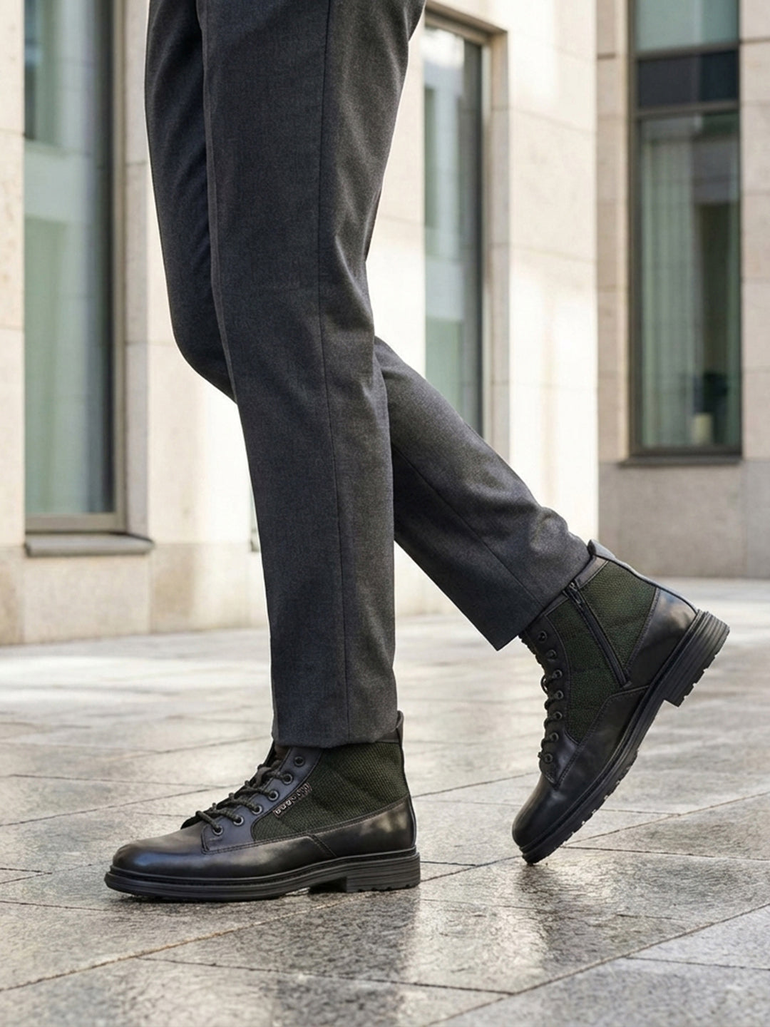 Lifestyle shot of bugatti Abel Black leather ankle boots with dark green textile detail, paired with gray dress pants.
