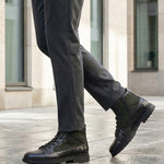 Lifestyle shot of bugatti Abel Black leather ankle boots with dark green textile detail, paired with gray dress pants.
