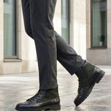 Lifestyle shot of bugatti Abel Black leather ankle boots with dark green textile detail, paired with gray dress pants.
