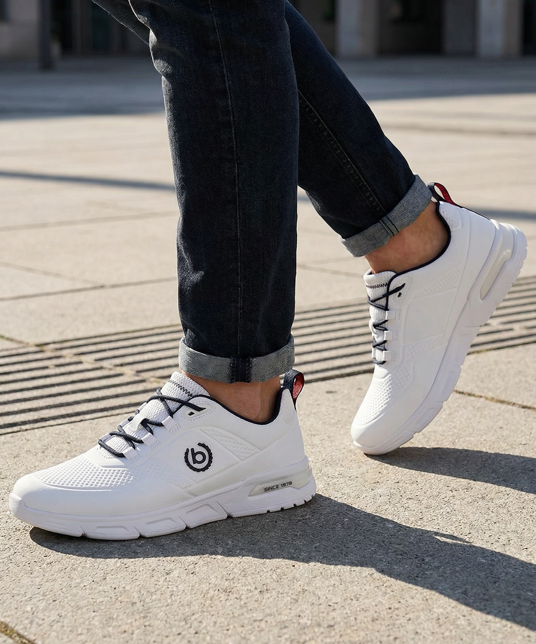 Lifestyle shot of the bugatti Nubola white sneakers, featuring black laces and logo detail, paired with dark denim jeans.
