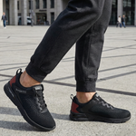 Lifestyle close-up of black bugatti Nubola comfort sneakers, with mesh texture and red heel accent, worn with dark gray sweatpants.
