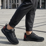 Lifestyle close-up of black bugatti Nubola comfort sneakers, with mesh texture and red heel accent, worn with dark gray sweatpants.
