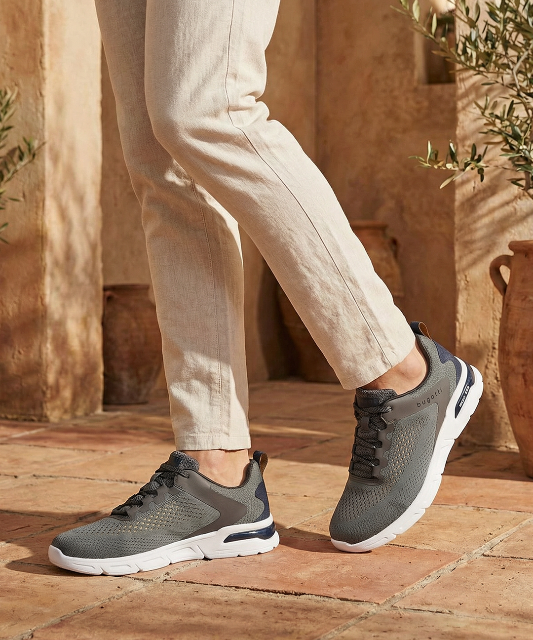 Lifestyle shot of bugatti Nubola dark gray sneakers with a white sole, paired with khaki-colored pants.
