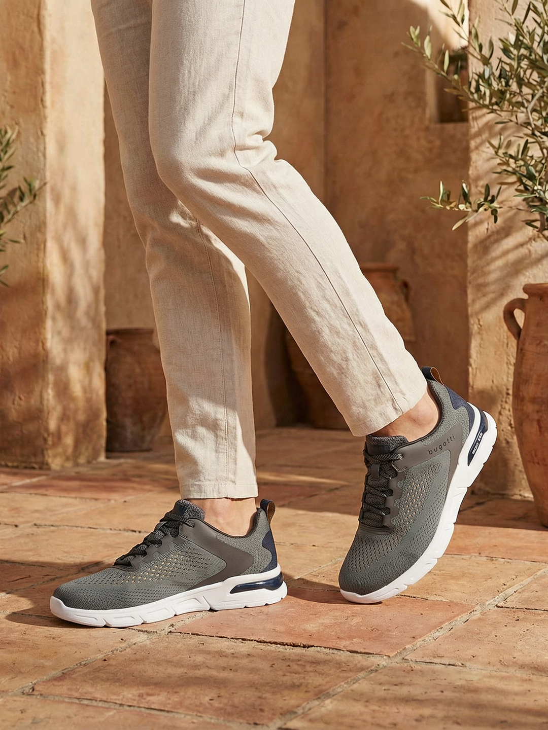 Lifestyle shot of bugatti Nubola dark gray sneakers with a white sole, paired with khaki-colored pants.
