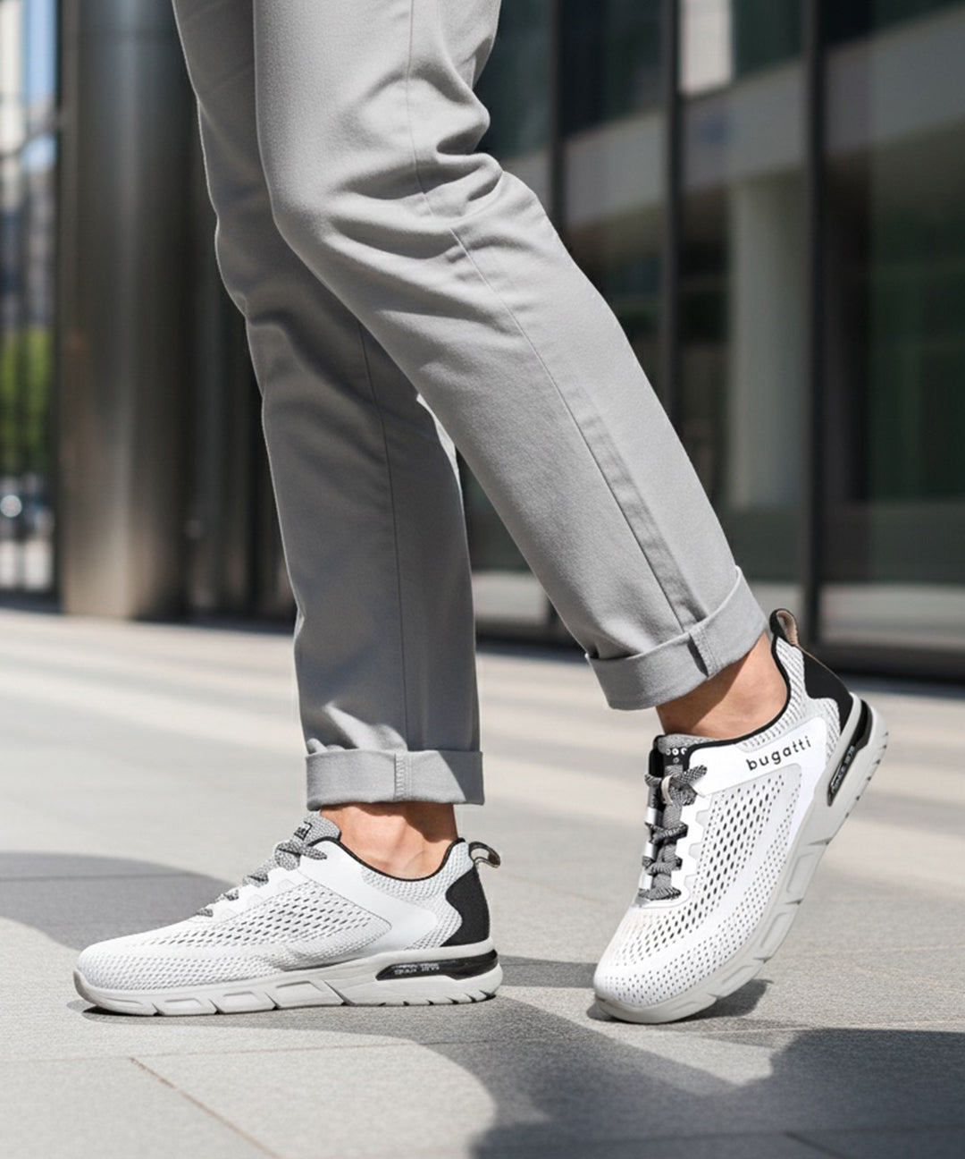 Cropped lifestyle shot of bugatti Nubola white sneakers with gray soles, black accents, and gray laces, worn with gray pants.