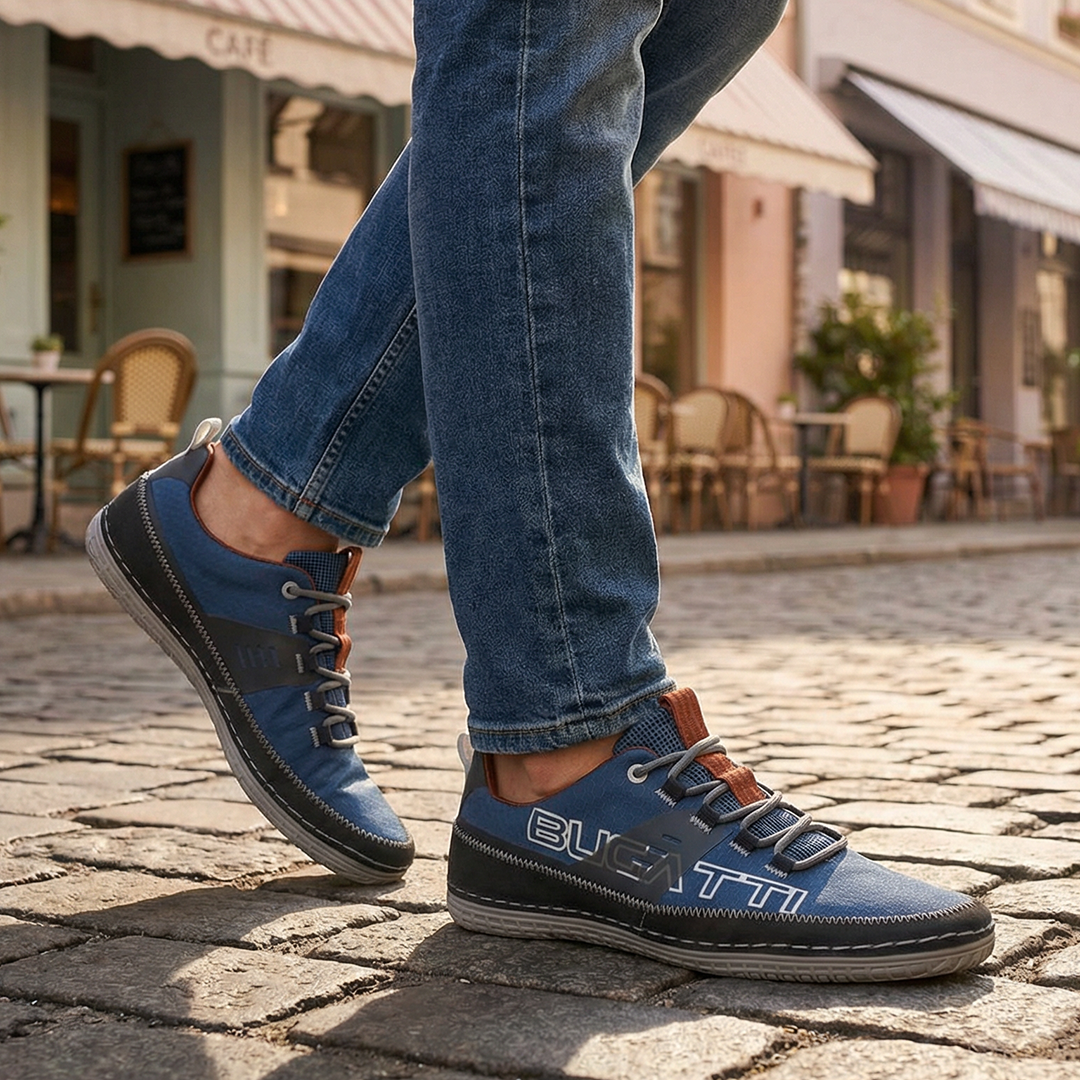 Lifestyle close-up of a person wearing blue denim jeans and bugatti Bimini blue low-top sneakers on a cobblestone street.