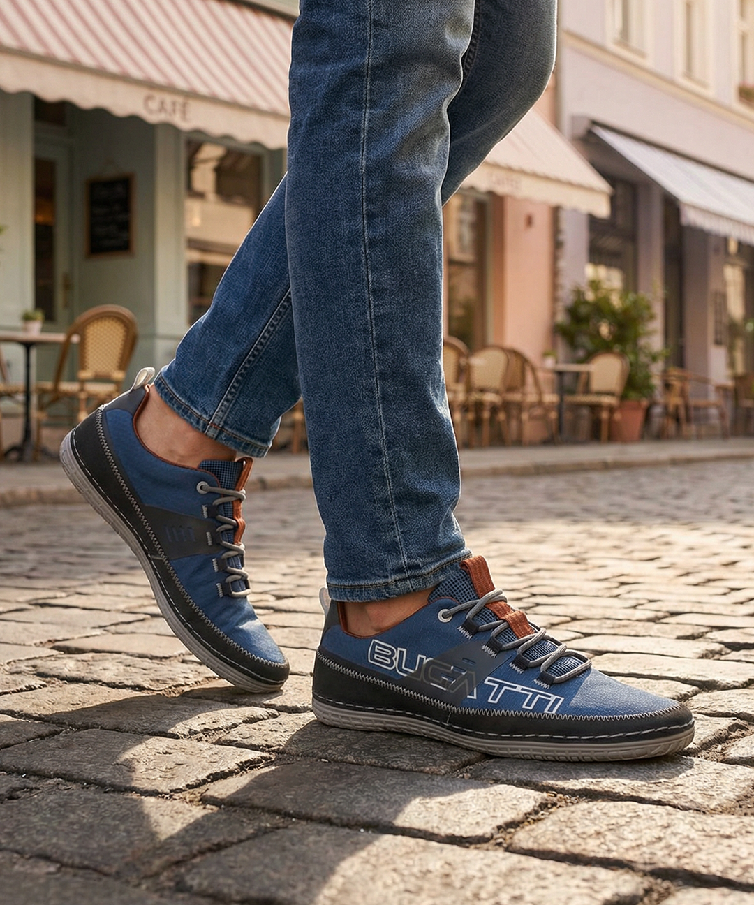 Lifestyle close-up of a person wearing blue denim jeans and bugatti Bimini blue low-top sneakers on a cobblestone street.