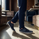 Lifestyle shot of bugatti Bimini dark blue low top sneakers with white soles, paired with blue trousers.
