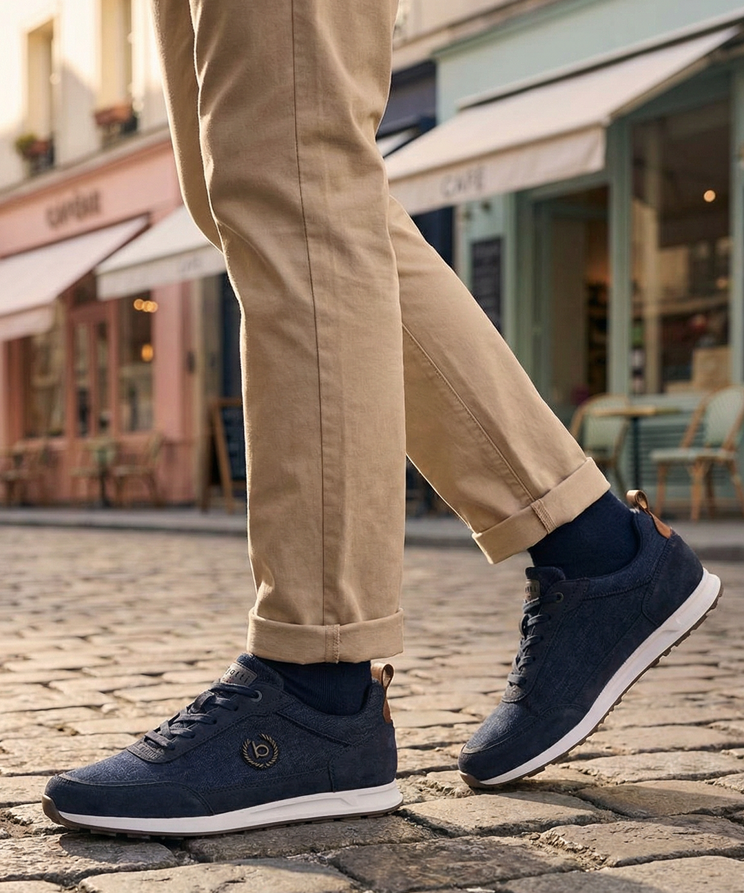 Lifestyle view of bugatti Ross dark blue sneakers with tan chinos and navy socks on a cobblestone street.
