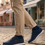 Lifestyle view of bugatti Ross dark blue sneakers with tan chinos and navy socks on a cobblestone street.
