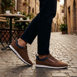 Lifestyle side view of the bugatti Ross Cognac Comfort Mid Top Sneakers, with blue accent and zipper detail, worn with black pants.
