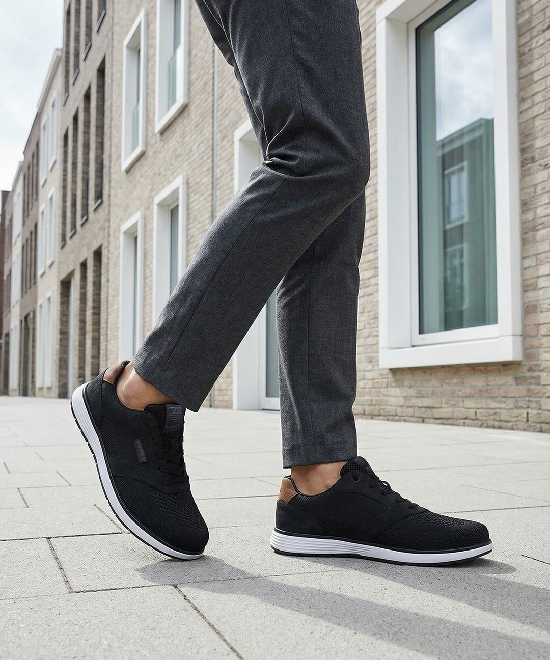 bugatti Baldini black sneakers, side view; low-cut with a white sole, worn with gray dress pants.
