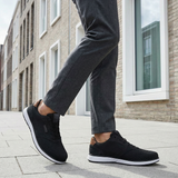 bugatti Baldini black sneakers, side view; low-cut with a white sole, worn with gray dress pants.