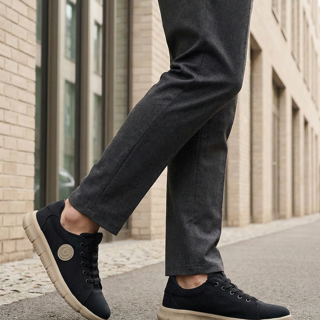 Lifestyle shot of bugatti Romer black canvas sneakers with beige soles, styled with gray dress pants.