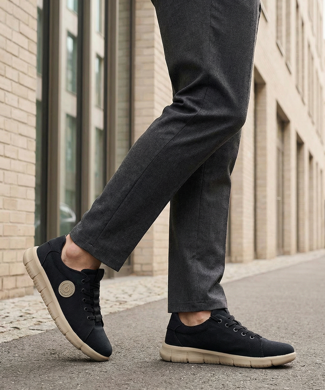 Lifestyle shot of bugatti Romer black canvas sneakers with beige soles, styled with gray dress pants.