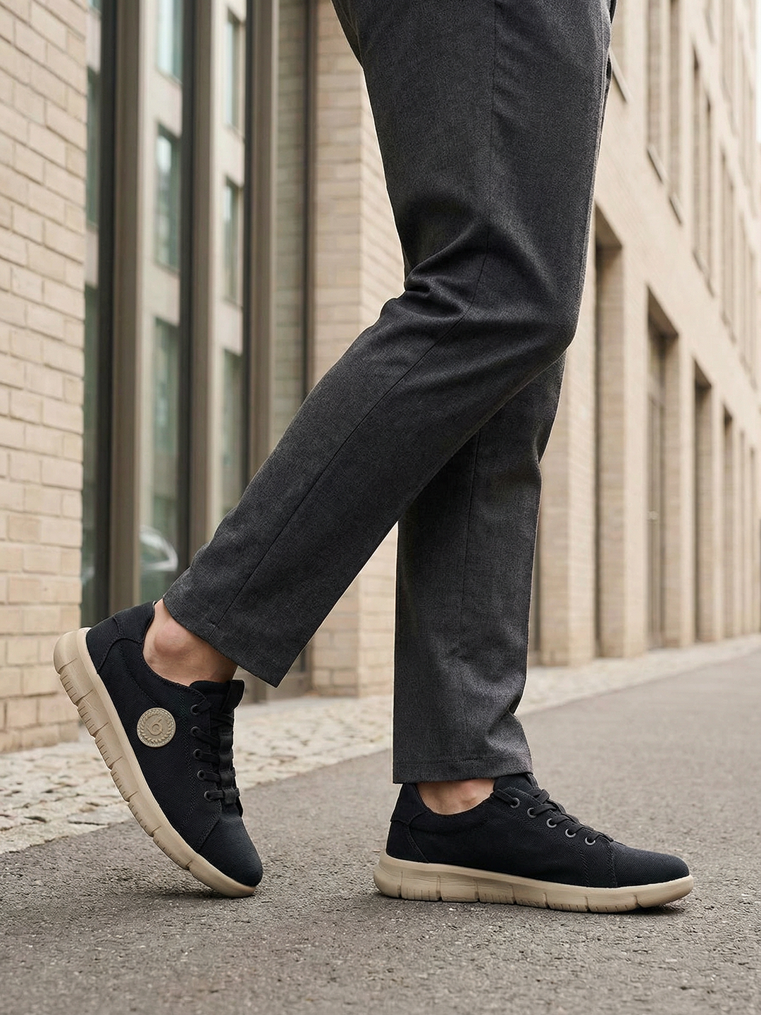 Lifestyle shot of bugatti Romer black canvas sneakers with beige soles, styled with gray dress pants.