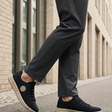 Lifestyle shot of bugatti Romer black canvas sneakers with beige soles, styled with gray dress pants.