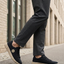 Lifestyle shot of bugatti Romer black canvas sneakers with beige soles, styled with gray dress pants.