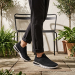 Lifestyle image of bugatti Yucatan black comfort sneakers, with white soles, worn with cuffed black pants.
