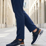 Lifestyle shot of bugatti Numbis dark blue athleisure sneakers with brown accents and white soles, paired with navy pants.
