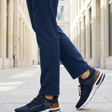 Lifestyle shot of bugatti Numbis dark blue athleisure sneakers with brown accents and white soles, paired with navy pants.
