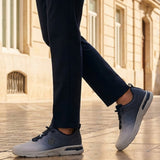 Lifestyle shot of bugatti Nubola light grey athleisure sneakers, with blue detailing, being worn with dark slacks.
