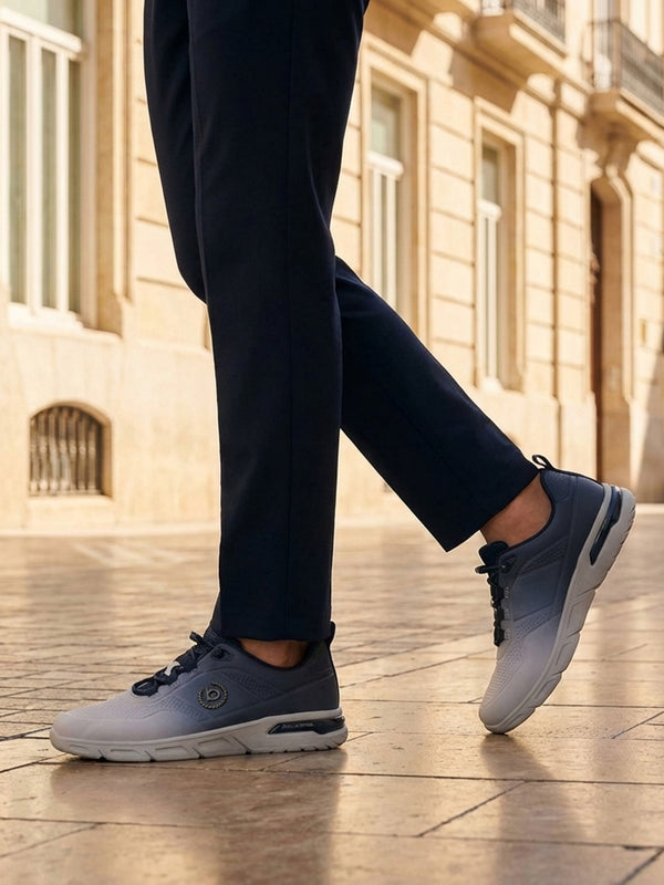 Lifestyle shot of bugatti Nubola light grey athleisure sneakers, with blue detailing, being worn with dark slacks.
