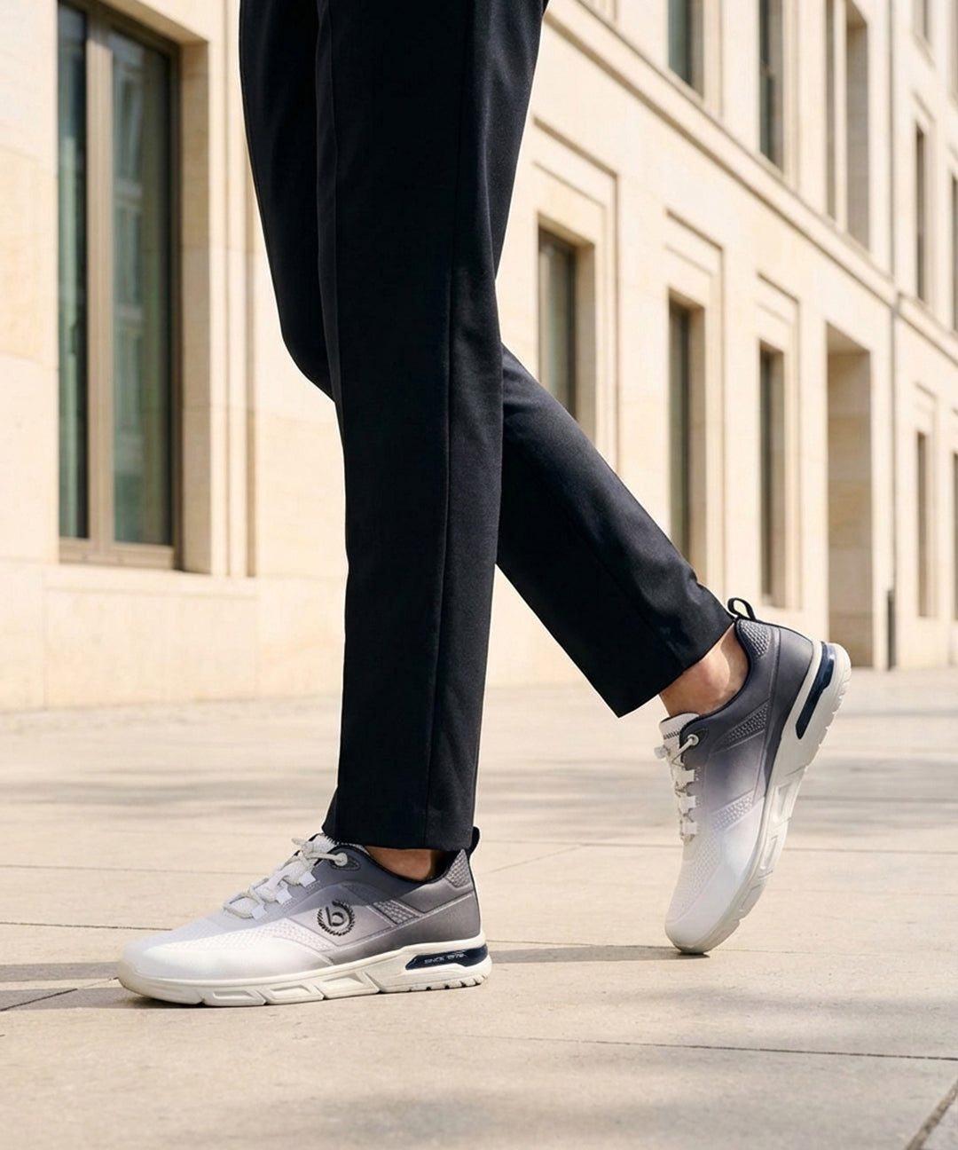 Cropped lifestyle view of bugatti Nubola white athleisure sneakers with a gradient design and white soles, worn with black trousers.
