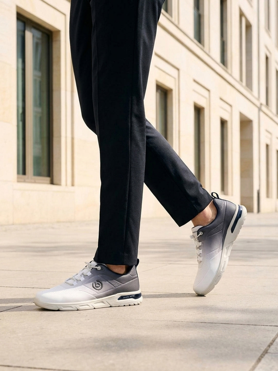 Cropped lifestyle view of bugatti Nubola white athleisure sneakers with a gradient design and white soles, worn with black trousers.
