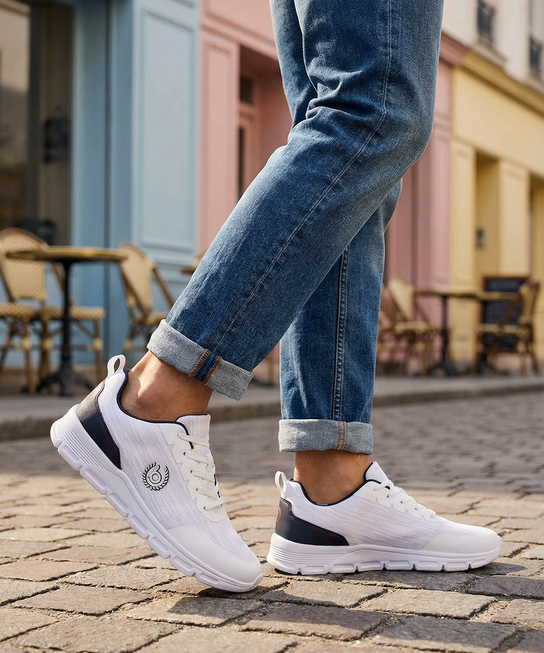 White comfort sneakers by bugatti with navy accents, shown with cuffed blue jeans on a cobblestone street.