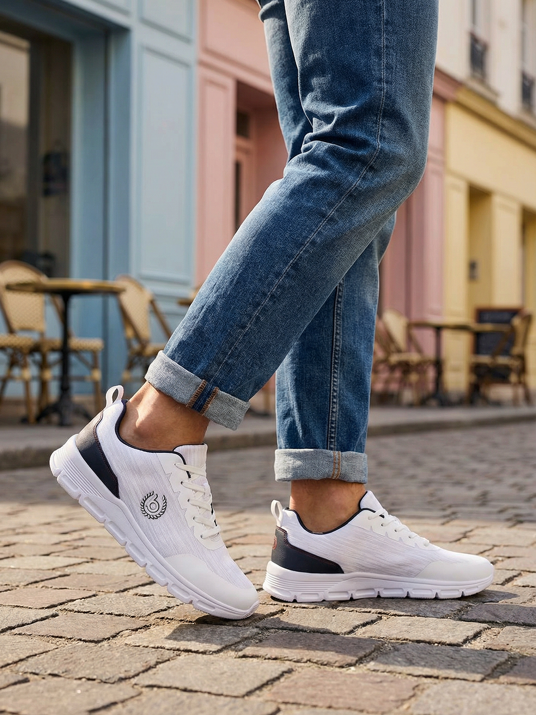 Lifestyle shot of bugatti Nexon white sneakers, with dark accents, worn with blue jeans on a brick surface.
