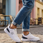 Lifestyle shot of bugatti Nexon white sneakers, with dark accents, worn with blue jeans on a brick surface.
