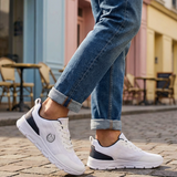 Lifestyle shot of bugatti Nexon white sneakers, with dark accents, worn with blue jeans on a brick surface.
