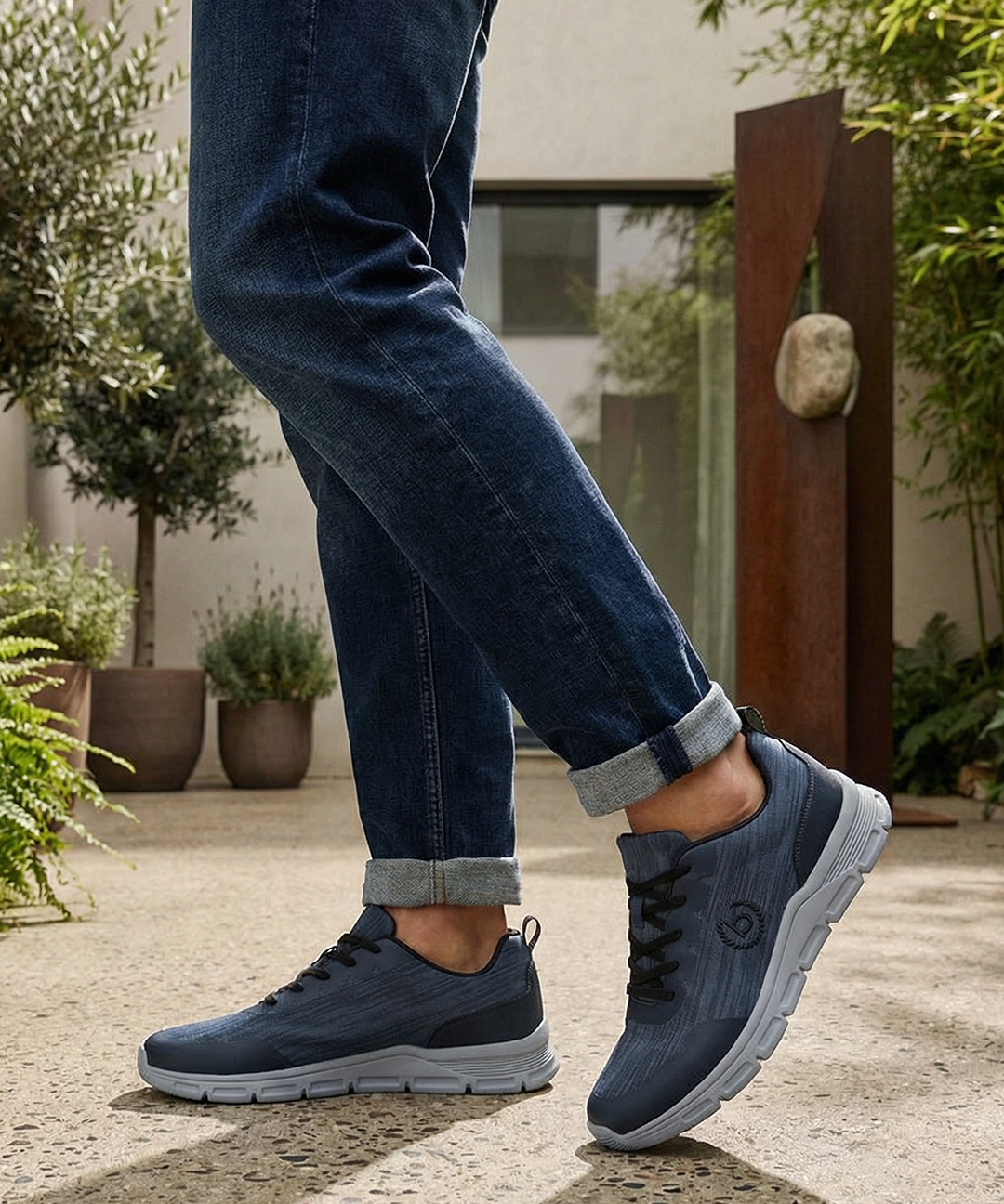 Lifestyle shot of bugatti Nexon blue sneakers with grey soles, worn with blue jeans and rolled cuffs.