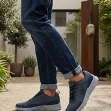 Lifestyle shot of bugatti Nexon blue sneakers with grey soles, worn with blue jeans and rolled cuffs.